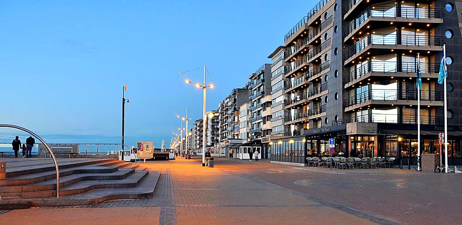 Der Deich und die Promenade von Koksijde in der Dämmerung, Gebäude am Meer an der belgischen Küste